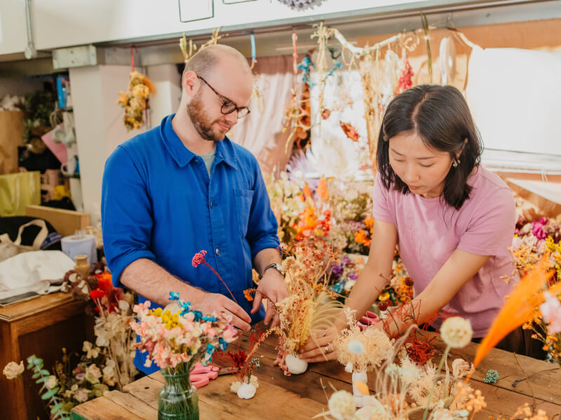 A woman is showing a man how to make an ikebana in a room full of flowers